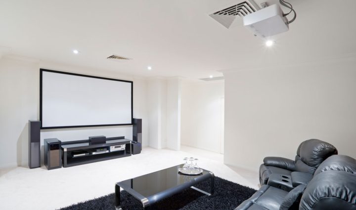A spacious home theater featuring a large screen with a projector setup and luxurious black leather recliners, perfect for movie nights and family entertainment.