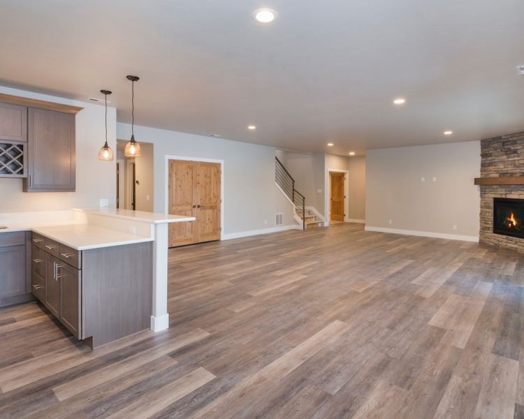 An expansive open-plan living area integrating a modern kitchen with a central island and a cozy living space with a stone fireplace, offering a perfect blend of functionality and warmth.