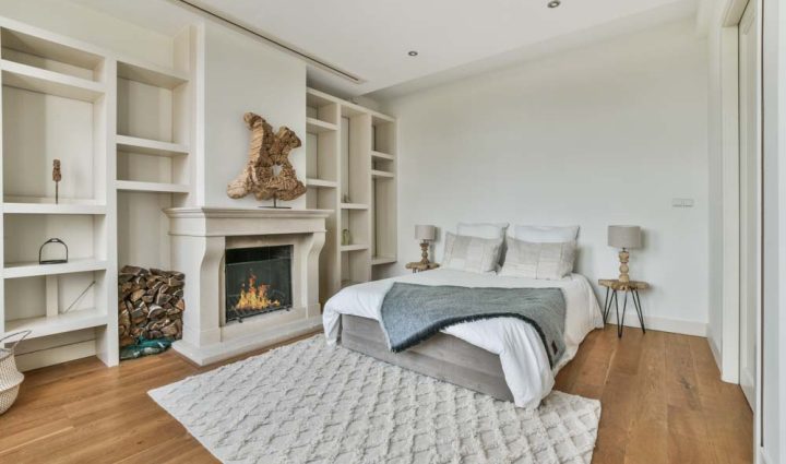 An elegantly designed bedroom showcasing a modern fireplace, surrounded by built-in shelving, with a serene and minimalist decor, complemented by a large comfortable bed.