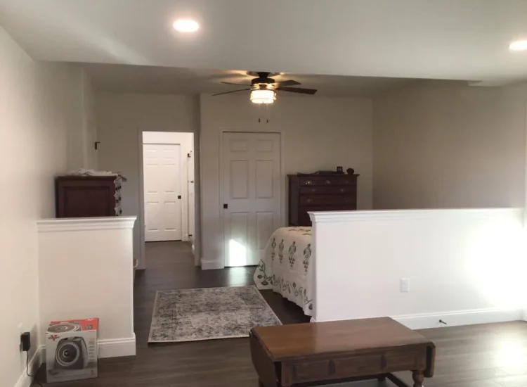A large, airy bedroom with a simple decor style, featuring a classic bed, hardwood floors, and a muted color palette, creating a tranquil sleeping environment.