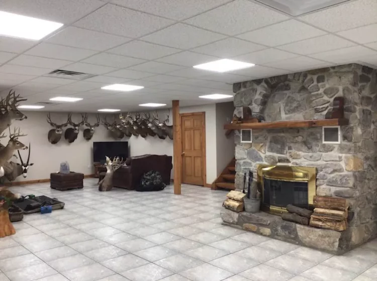 Large basement converted into a trophy room with stone fireplace, displaying a collection of mounted deer heads, providing a rustic recreational space.