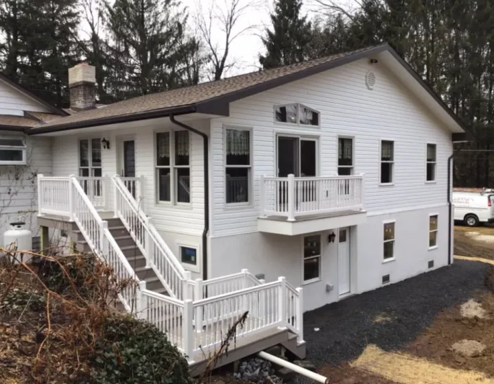 A stylish home addition featuring white siding and balcony, with a modern design that contrasts with the natural surroundings.