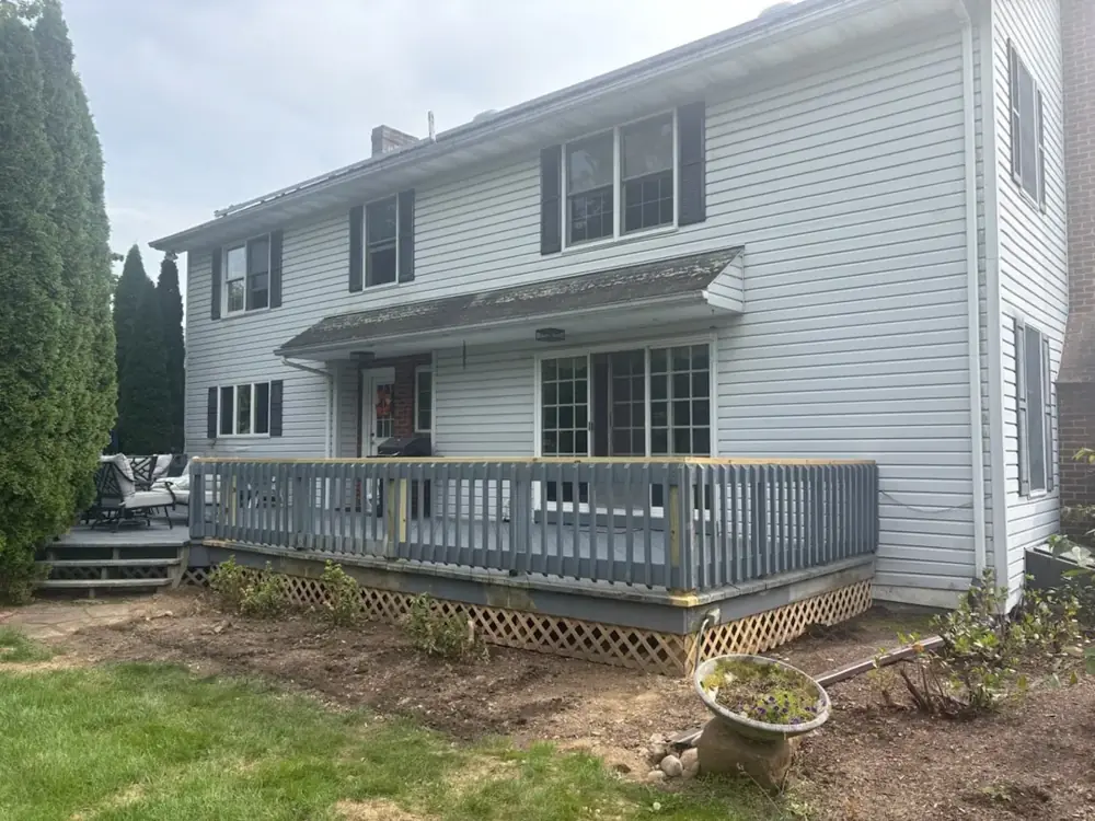 Rear view of a two-story home with a gray deck featuring a rebuilt railing, new top caps and lattice skirting.
