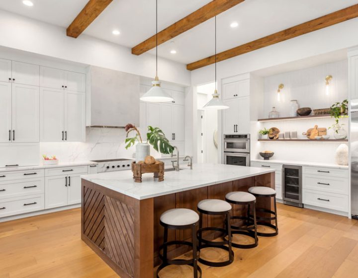 A spacious kitchen showcasing a large center island with seating, white cabinetry, and wooden beams, combining rustic charm with modern design.